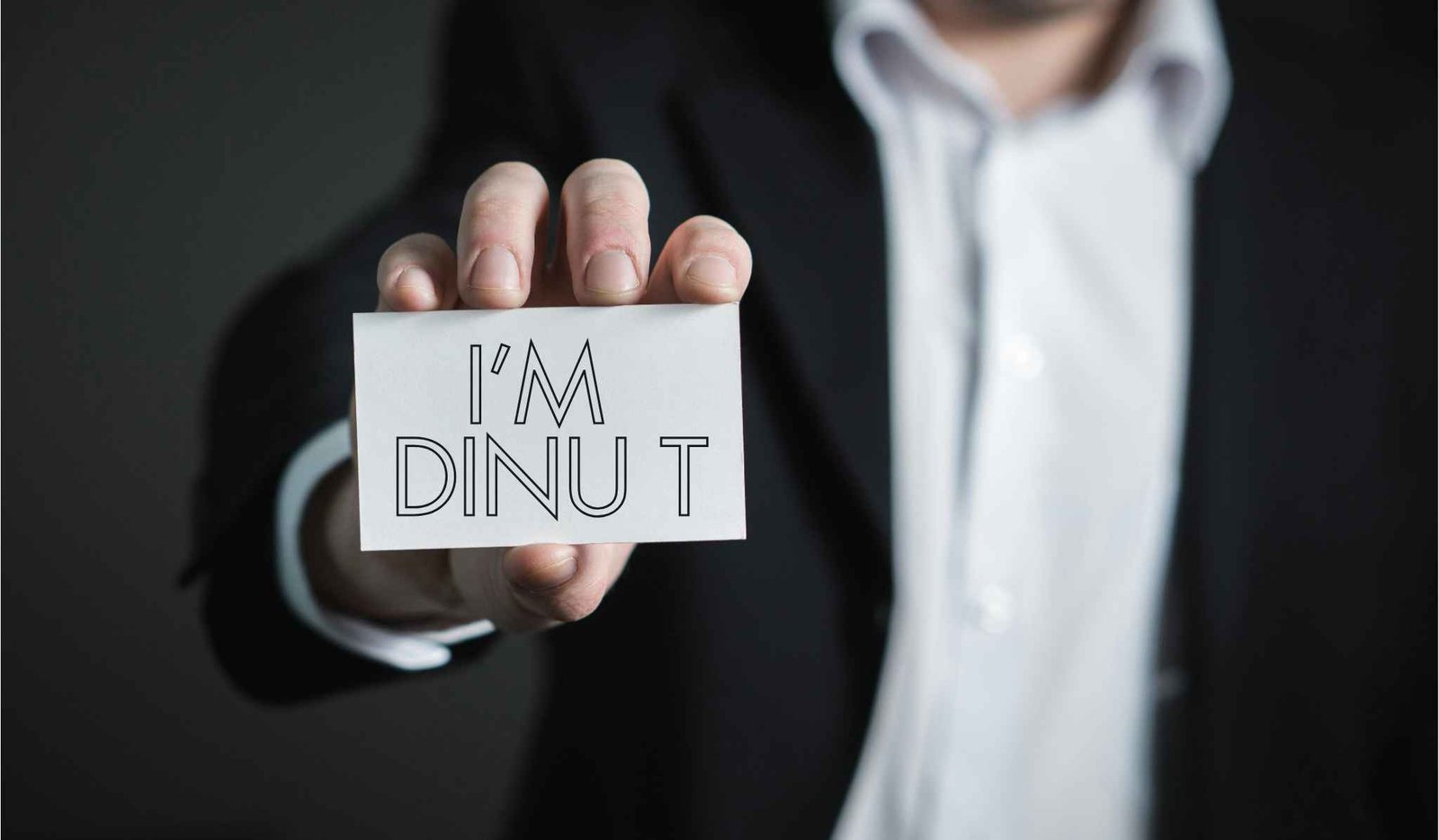 i’m dinu t a man with suit sand coat showing a visiting card with text freelance-digital-marketer-in-kollam